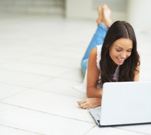 Portrait of attractive young woman lying down and using a laptop